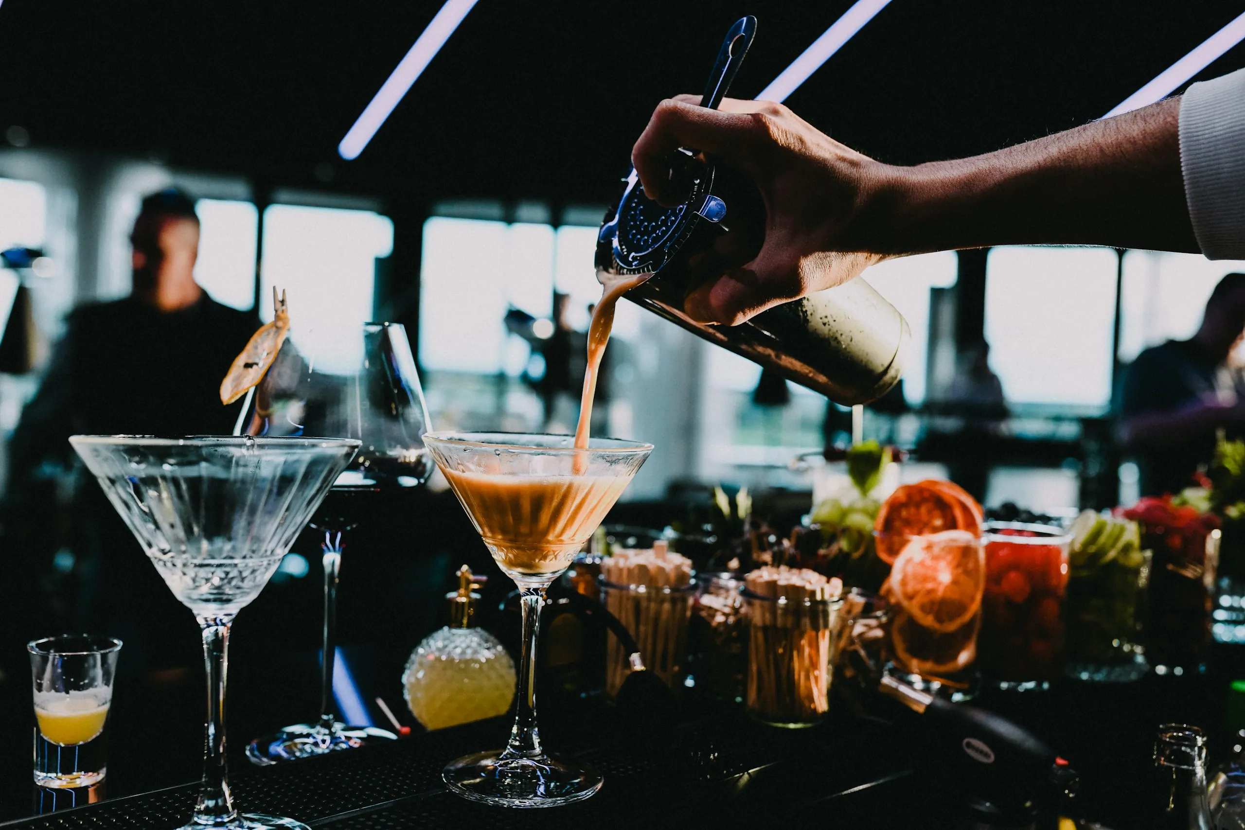 A bartender pours a drink from a shaker into a glass at a bar counter